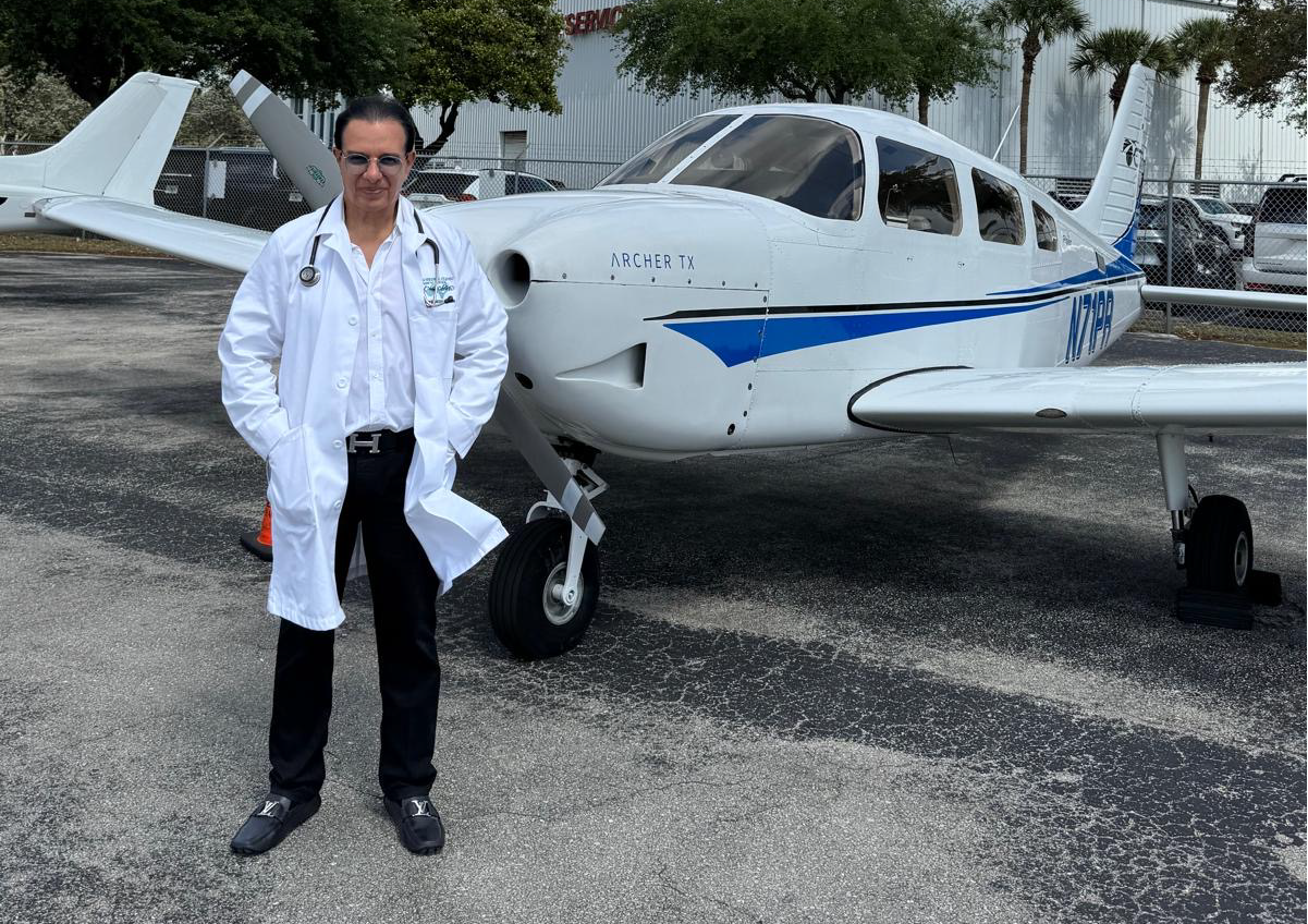 Dr. Phanor Calle standing beside a white single-engine airplane during aviation medical exam session