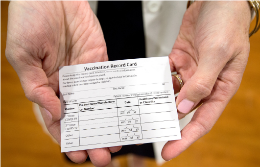 Hands holding a vaccination record card for USCIS Immigration Medical Exam